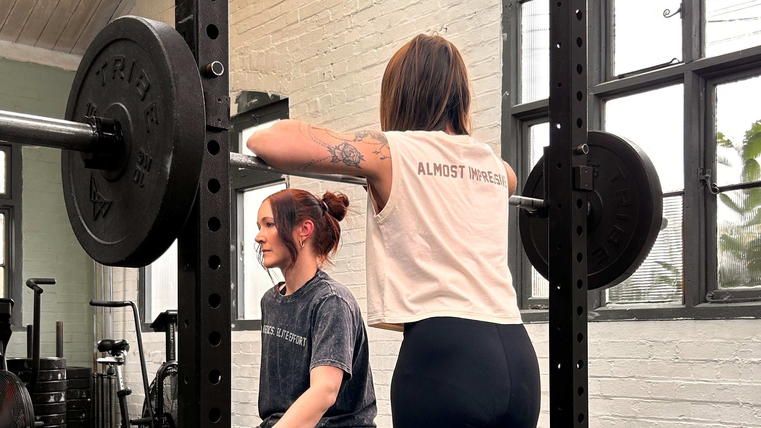 Two women working out with a barbell in a gym setting.