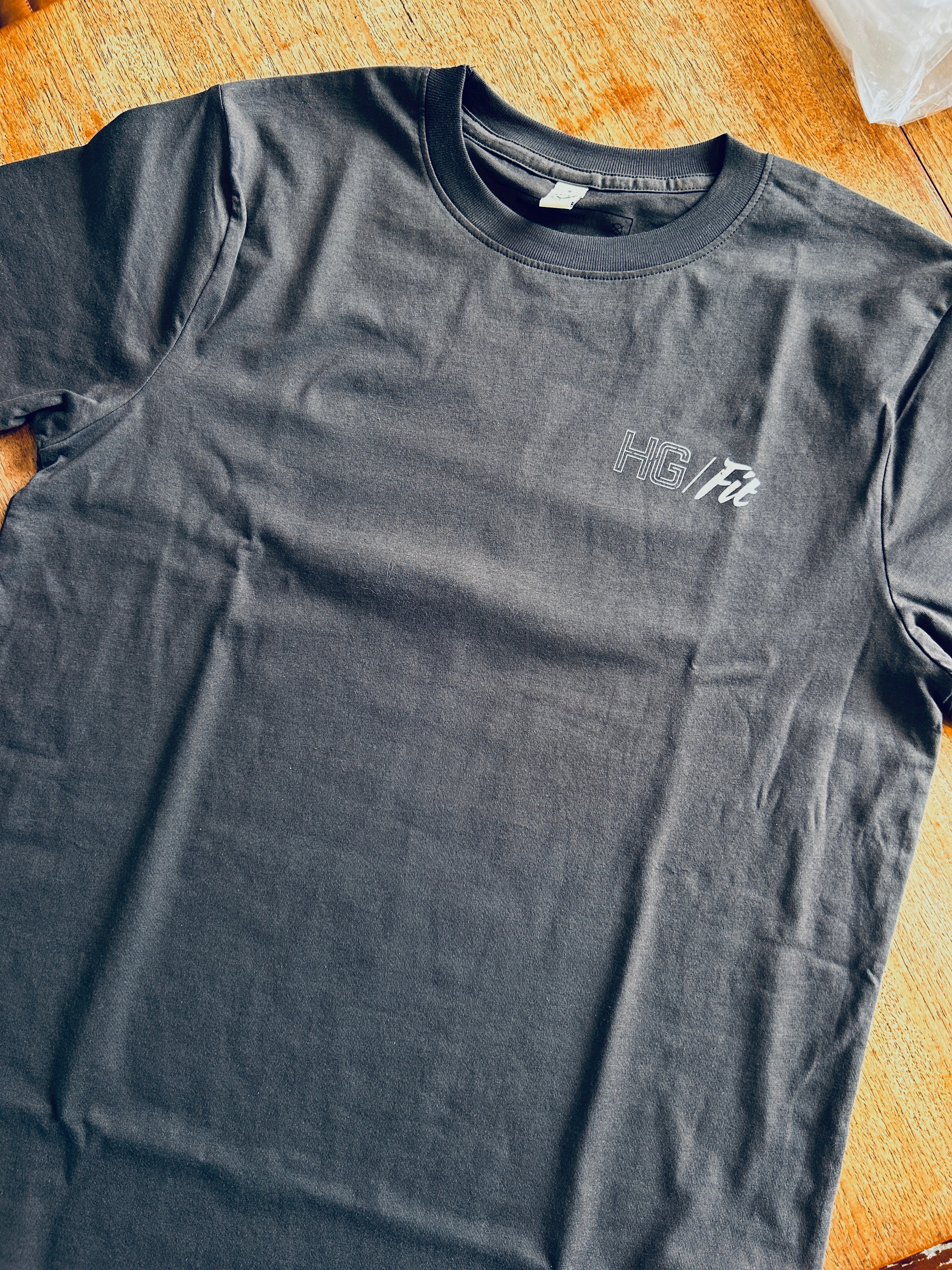 Gray t-shirt with 'HG Fit' logo on a wooden surface